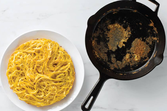 An empthy skillet and a dish filled with spaghetti, ready to be served.