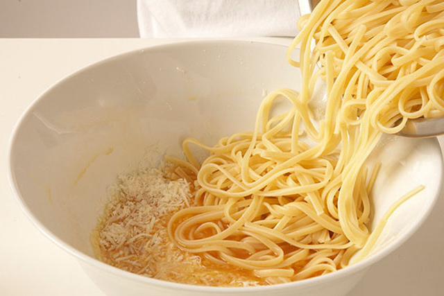 Eine Person schüttet Spaghetti in eine Schüssel mit Eiern.