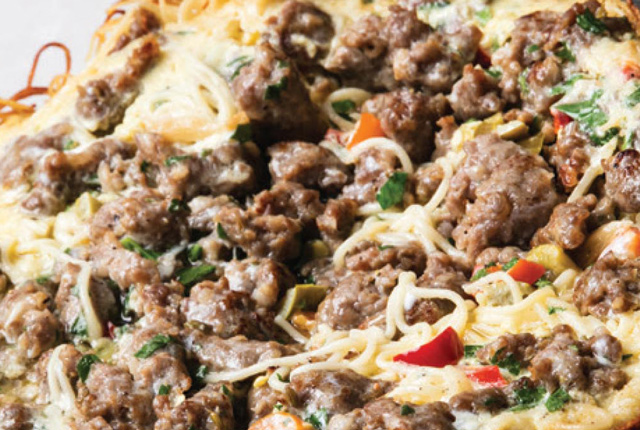 Eine Nahaufnahme einer Wurst-Pasta-Frittata, die eine Auflaufform mit Fleisch und Gemüse zeigt.