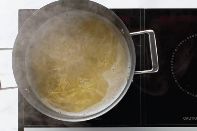 Spaghetti werden in einer Pfanne auf einem Herd zubereitet.