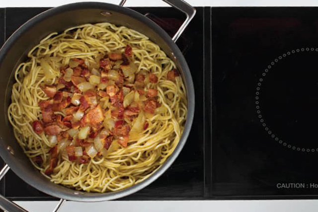 Eine Pfanne mit Spaghetti, Zwiebeln und Speck. Das sind die letzten Zutaten von SPAGHETTI Carbonara.