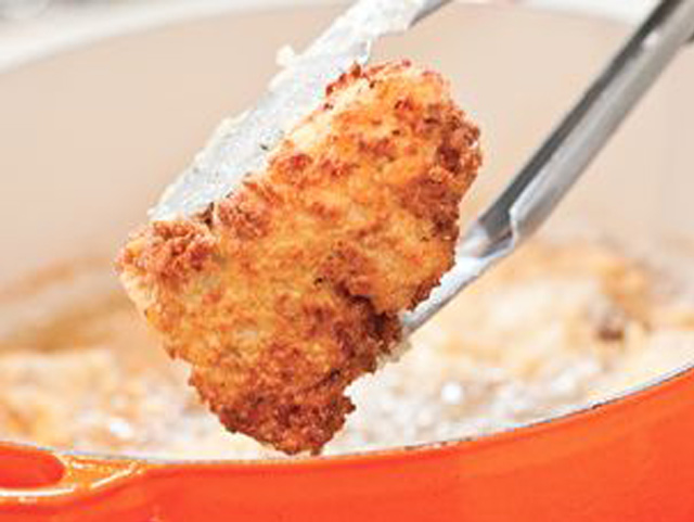 Eine Hand hält einen Löffel über eine Bratpfanne und präsentiert Extra Crispy Fried Chicken