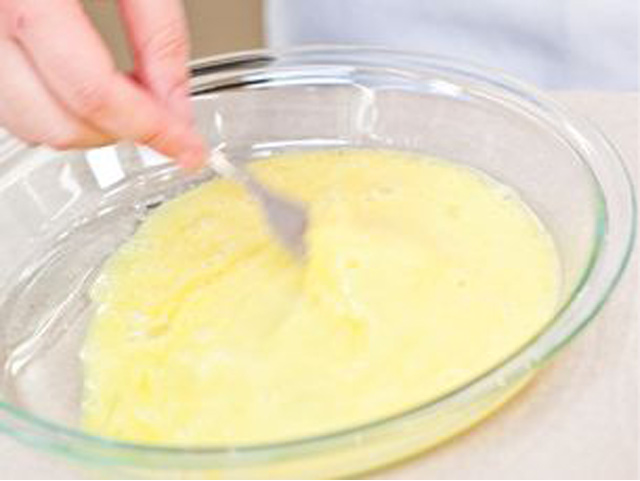 A person is stirring yellow batter in a bowl, showcasing a blend of ingredients for cooking Hähnchenschnitzel knusprig.