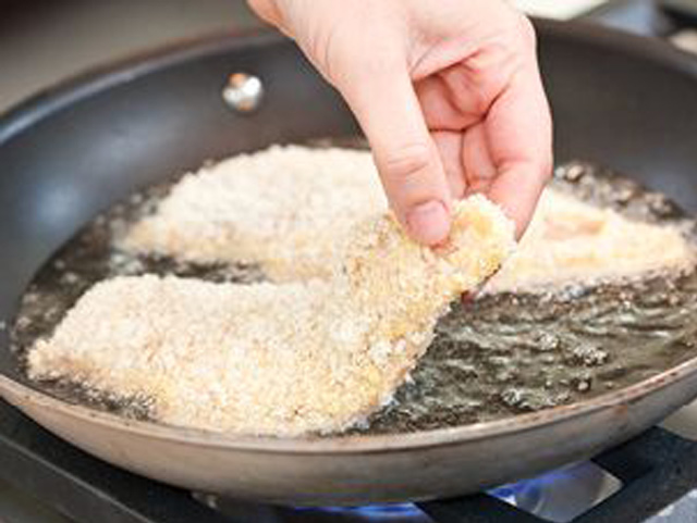 Die Hand einer Person brät gekonnt Hähnchenschnitzel in einer Pfanne und zeigt so den Kochvorgang in einer Küchenumgebung.