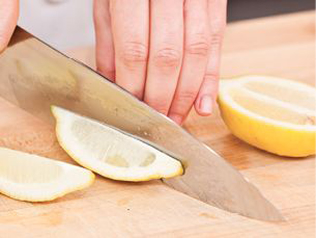 Eine Person schneidet geschickt eine frische Zitrone mit einem scharfen Messer auf einem hölzernen Schneidebrett in zwei Hälften.