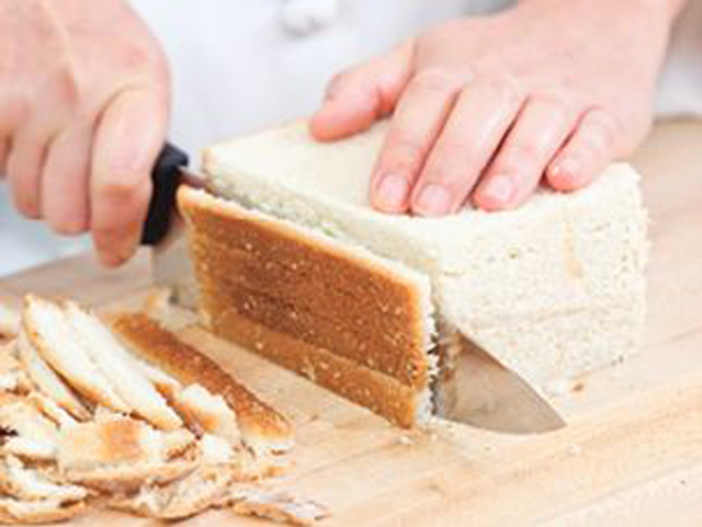 Eine Person schneidet geschickt mit einem scharfen Messer einen Laib Brot auf einem hölzernen Schneidebrett.