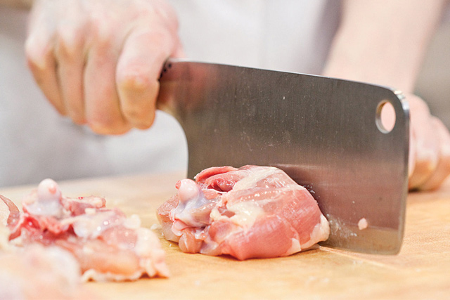 Eine Person schneidet Hühnchen mit einem großen, breiten Messer in kleine Stücke