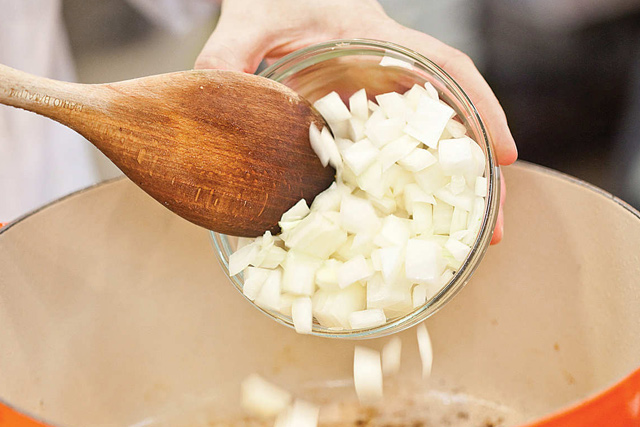 Bereiten Hühnerfond Sie es vor, indem Sie in kleine Würfel geschnittene Zwiebeln in den Topf geben