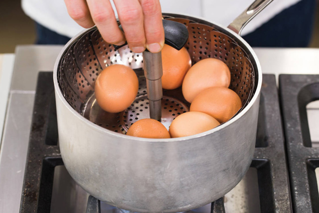 Eine Person hält einen Topf mit Eiern in der Hand, bereit zum Kochen.