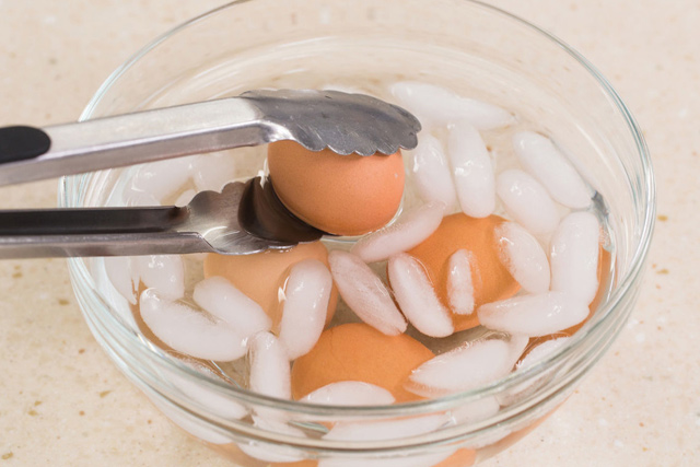 Eine Person verwendet eine Zange, um Eier aus einem Eiswürfel zu entnehmen.