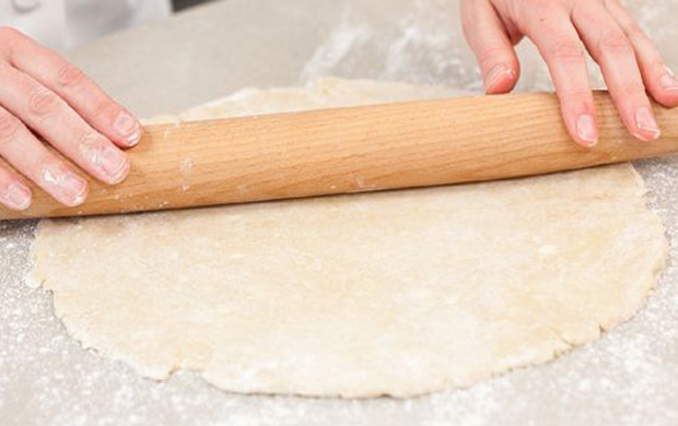 Eine Person rollt sorgfältig Teig auf einem Tisch aus, um ihn für das Backen vorzubereiten.