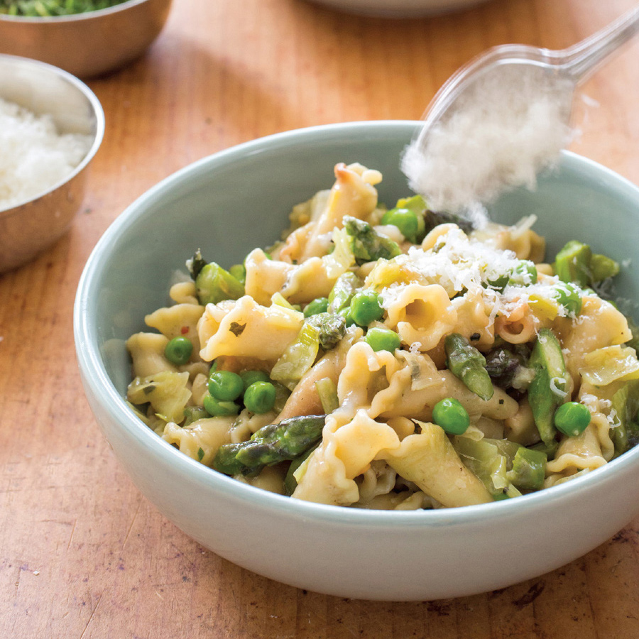 Zwei Schüsseln Pasta Primavera mit Erbsen und Spargel garniert.