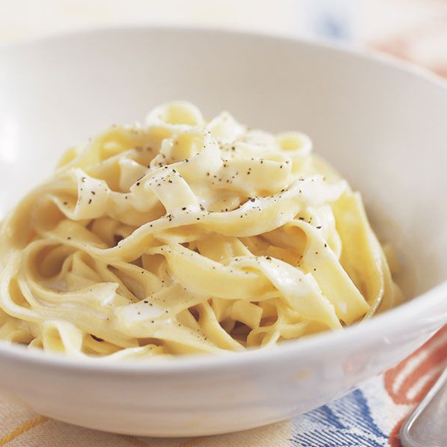 Eine ansprechende Schüssel Fettuccine Alfredo, serviert mit einem Löffel und einer Gabel.