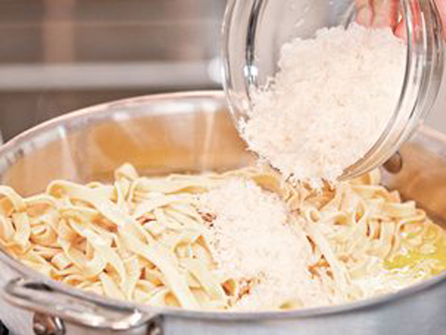 Jemand füllt Fettuccine Alfredo in einen Topf, um eine leckere Pasta-Mahlzeit zu kochen.