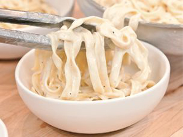 Fettuccine Alfredo in einer Schüssel, die mit einer Zange festgehalten wird, um die Nudeln zu portionieren.