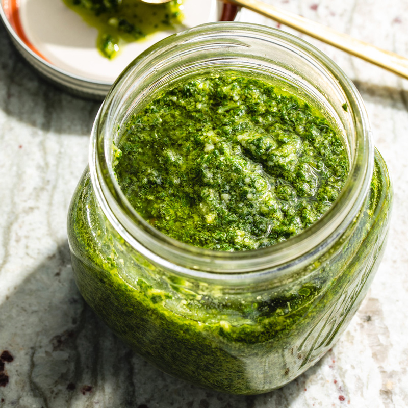 Ein Glas mit frischem Basilikum Pesto, das reich an grüner Farbe und aromatischen Kräutern ist.