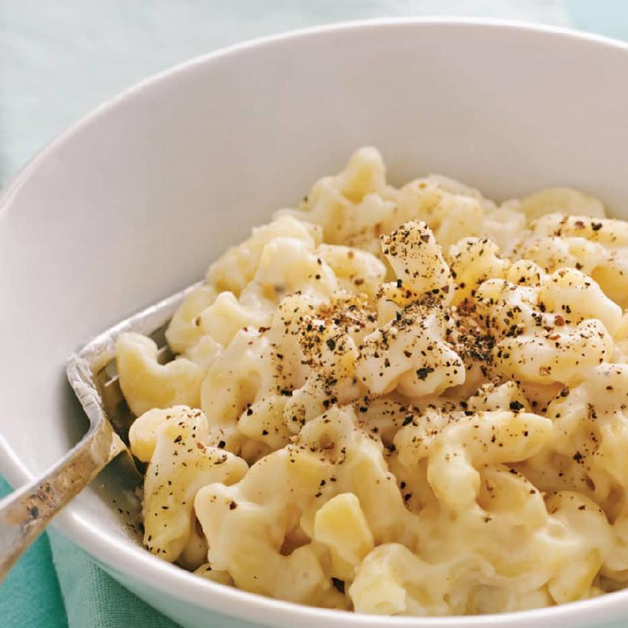 Cremiger Mac and Cheese in einer weißen Schüssel mit einem silbernen Löffel.