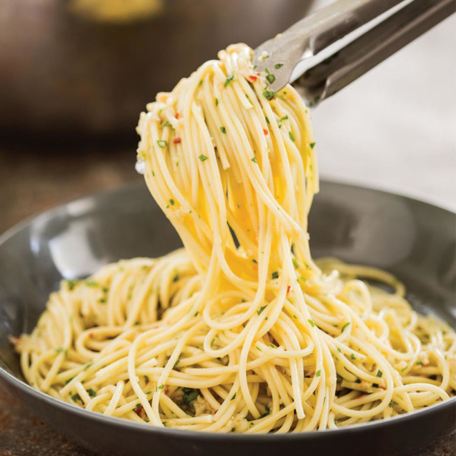 Eine Gabel nimmt Spaghetti aglio e olio aus einem Topf auf einem Herd.